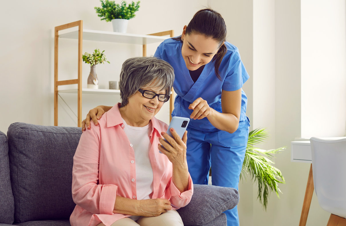 Elderly woman holding a phone while caregiver points out something